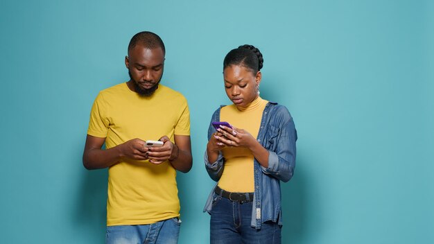 스마트폰을 사용하여 스튜디오에서 문자 메시지를 보내는 아프리카계 미국인 부부. 현대 남성과 여성이 기술로 휴대전화 화면을 보고 있습니다. 인터넷에서 함께 재미있는 활동을 즐기는 사람들.