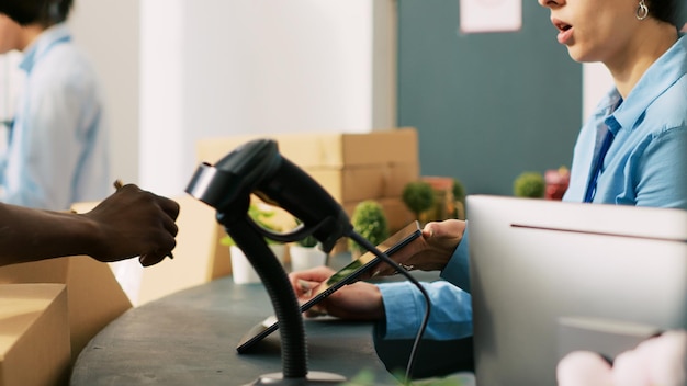 African american courier signing distribution report on tablet computer, discussing online orders details with store manager in modern boutique. Employee preparing fashionable clothes for shipping