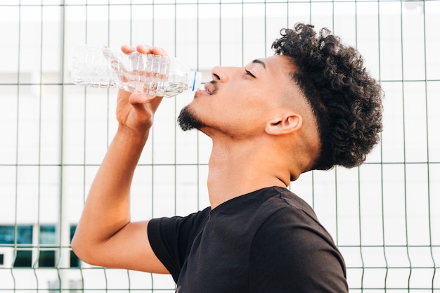 African American delighted male drinking water at stadium