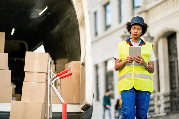 African American deliverer using digital tablet while unloading packages from a van