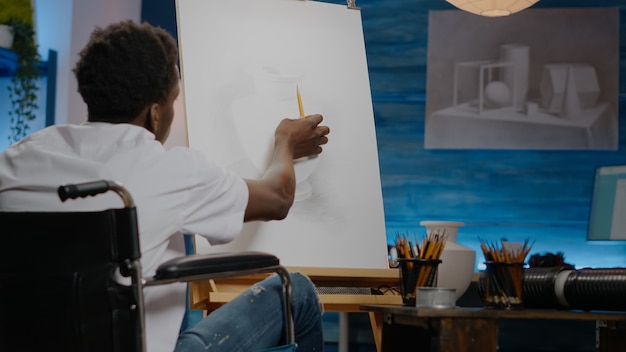 Афро-американский молодой художник-инвалид рисует вазу на холсте