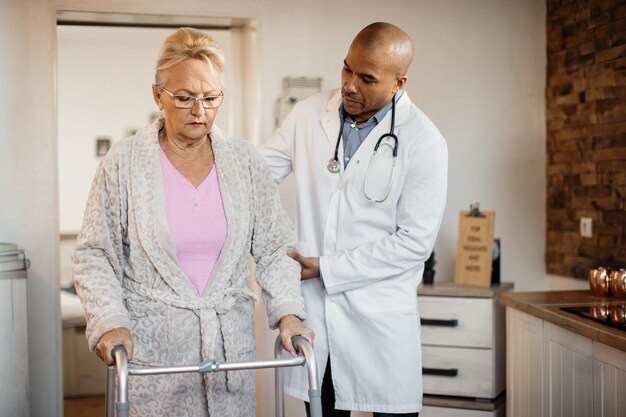 African American doctor assisting senior woman in using mobility walker at nursing home