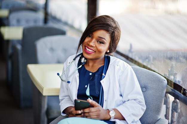 African american doctor female with stethoscope looked at phone and sitting on clinic