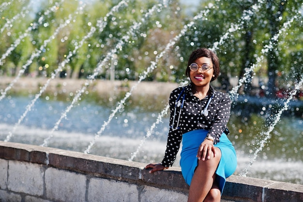 Африканская женщина-врач со стетоскопом позирует на фоне фонтанов на открытом воздухе