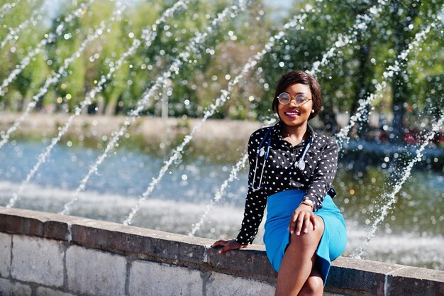 Африканская женщина-врач со стетоскопом позирует на фоне фонтанов на открытом воздухе