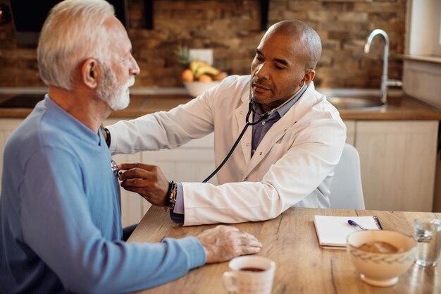 African American doctor listening senior man's heartbeat during home visit