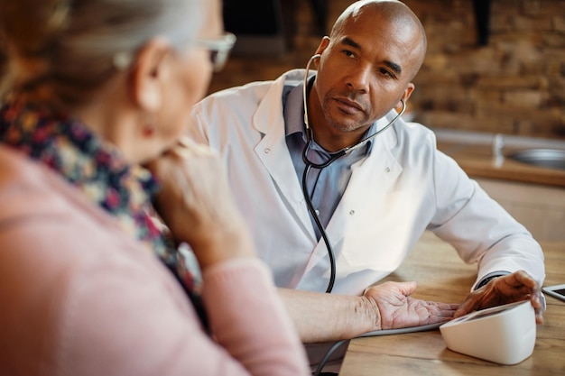 African American doctor measuring blood pressure of senior patient at nursing home