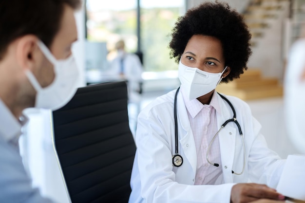 クリニックで患者と話している間保護フェイスマスクを身に着けているアフリカ系アメリカ人の医師