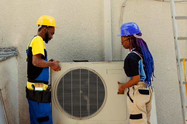 African american engineering coworkers opening up rusty out of service air conditioner to replace it with new performant outside condenser after draining refrigerant and replacing ductwork