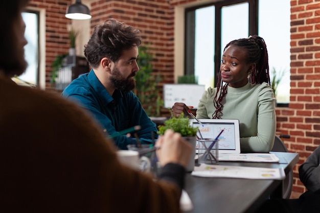 African american entrepreneur woman showing marketing statistics to businesspeople explaining company turnover during business meeting in startup office. Diverse team working at financial project