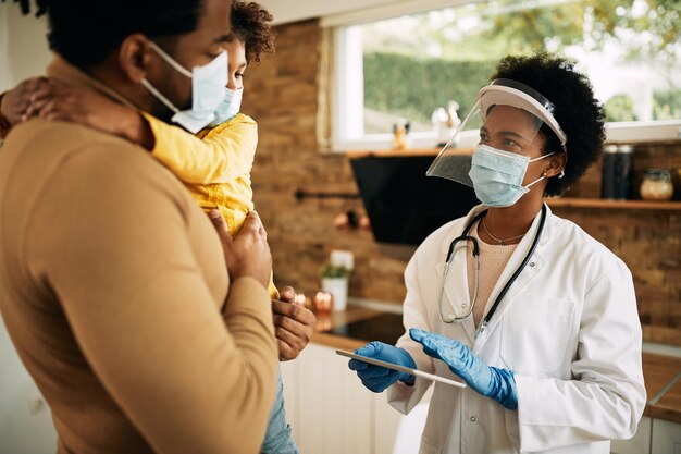 African American family doctor communicating with father and daughter during home visit