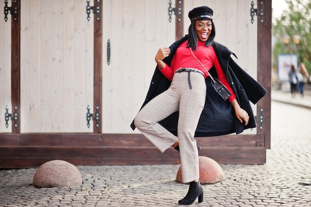 Free photo african american fashion girl in coat and newsboy cap posed at street