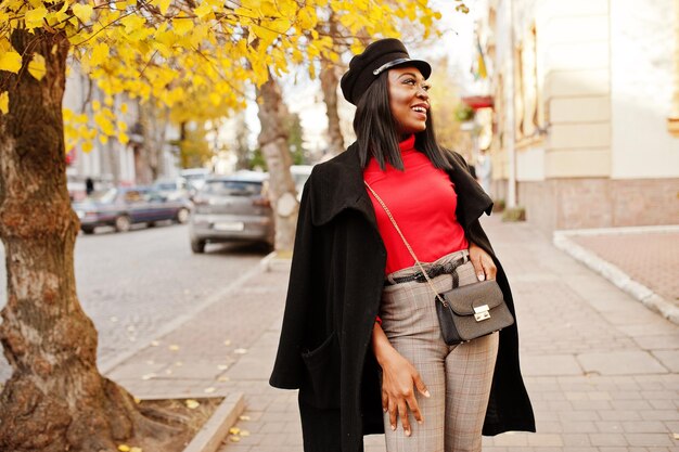 코트와 신문 모자를 쓴 아프리카계 미국인 패션 소녀가 거리에서 포즈를 취했습니다.