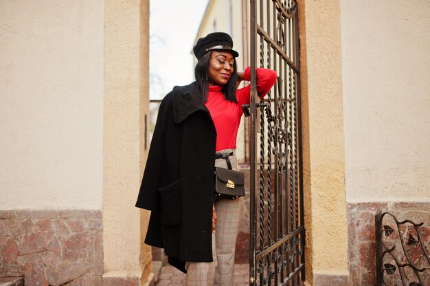 Ragazza di moda afroamericana in cappotto e berretto da strillone poste in strada