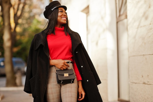 코트와 신문 모자를 쓴 아프리카계 미국인 패션 소녀가 거리에서 포즈를 취했습니다.