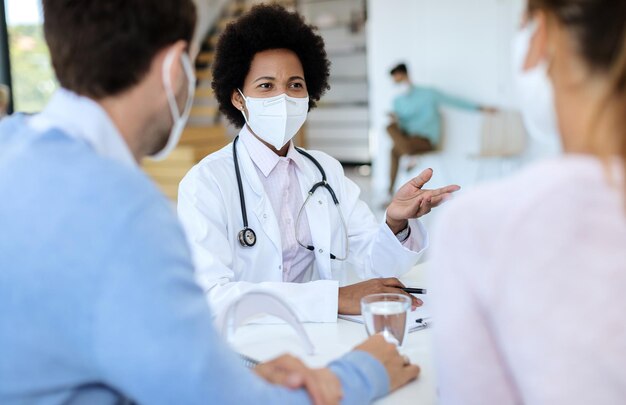 Афроамериканская женщина-врач консультируется с парой во время эпидемии коронавируса