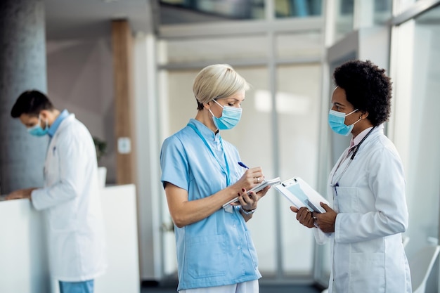 Medico femminile afroamericano che parla con un'infermiera in un corridoio della clinica medica