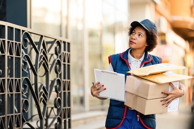 African American female postal worker carrying packages while delivering them in residential district