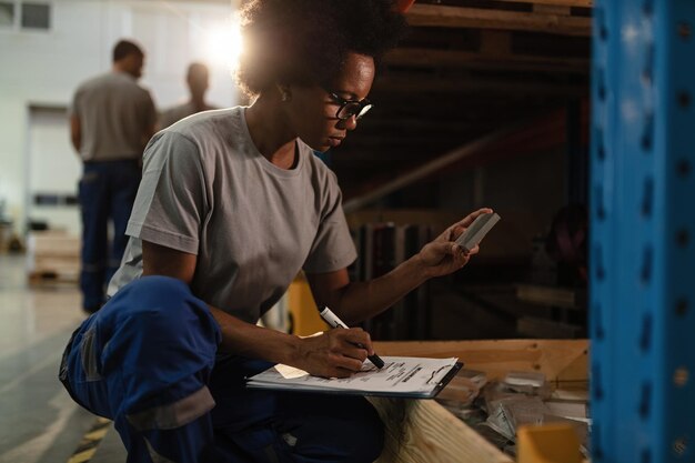 African American female worker checking products before the shipment and taking notes in a warehouse