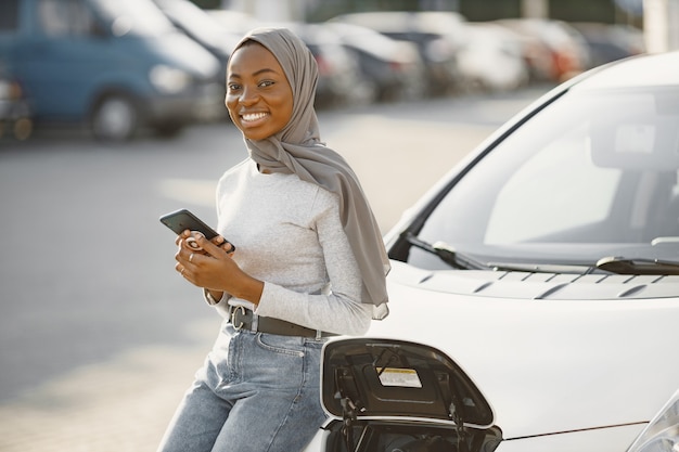 電気ガソリンスタンドで電気自動車を充電するアフリカ系アメリカ人の女の子