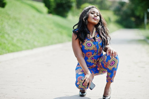 Free photo african american girl in coloured clothes sat down with mobile phone outdoor fashionable black woman