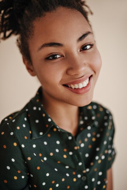 베이지색 배경에 격리된 밝은 곱슬머리 젊은 여성의 스튜디오 샷으로 진지한 미소로 포즈를 취한 아프리카계 미국인 소녀
