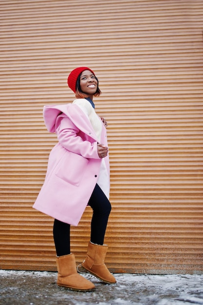 Ragazza afroamericana con cappello rosso e cappotto rosa contro persiane arancioni