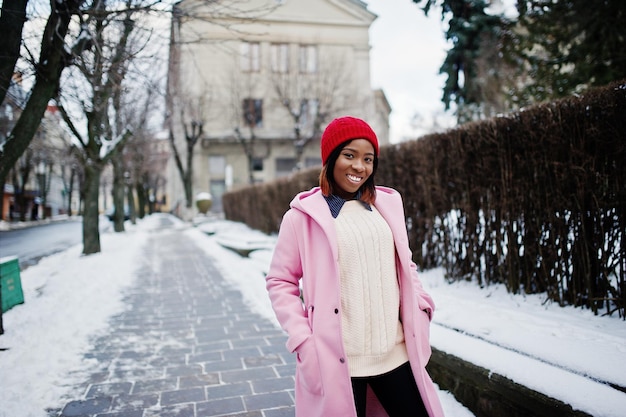 African american girl in red hat and pink coat at street of city on winter day