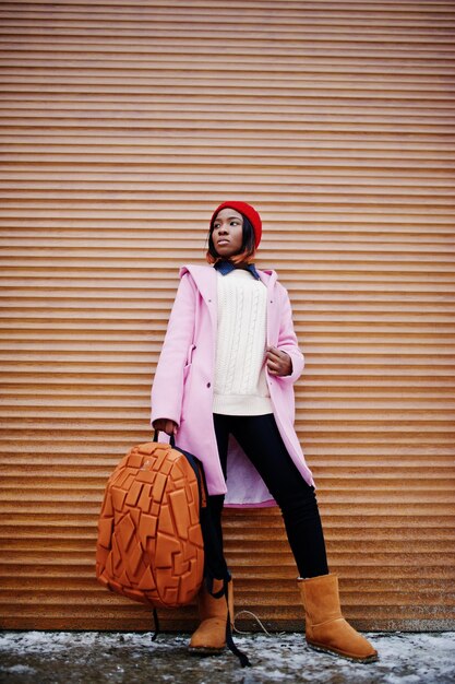 African american girl in red hat and pink coat with backpack against orange shutters