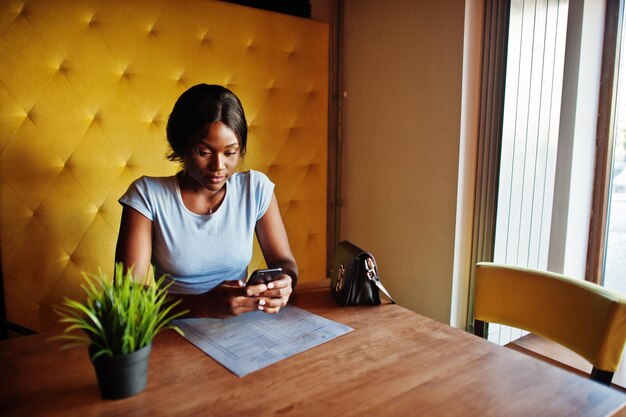 Африканская американка сидит в кафе с мобильным телефоном