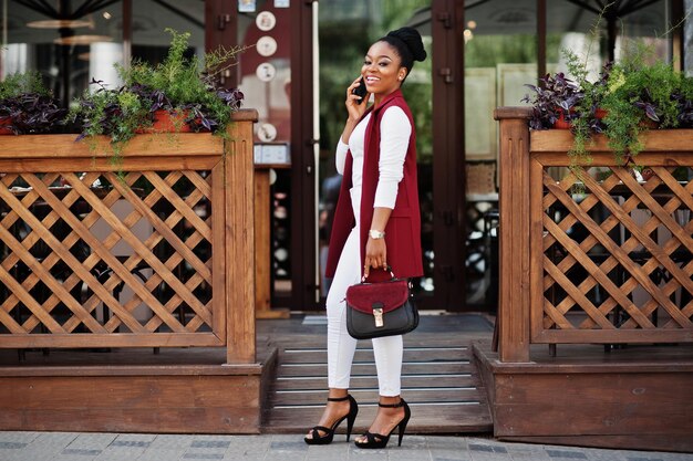핸드백을 든 아프리카계 미국인 소녀가 steets city 야외에서 포즈를 취하고 전화 통화를 합니다.