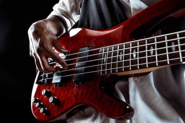 African American handsome jazz musician playing bass guitar in the studio on a black background. Music concept. Young joyful attractive guy improvising. Close-up retro portrait.