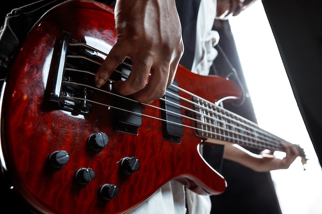 African American handsome jazz musician playing bass guitar in the studio on a black background. Music concept. Young joyful attractive guy improvising. Close-up retro portrait.