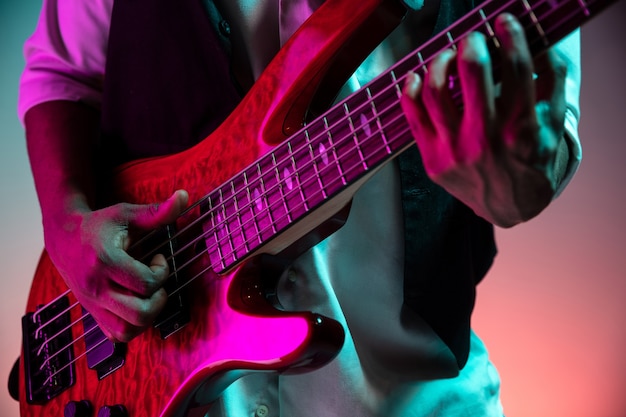 Free photo african american handsome jazz musician playing bass guitar in the studio on a neon background. music concept. young joyful attractive guy improvising. close-up retro portrait.