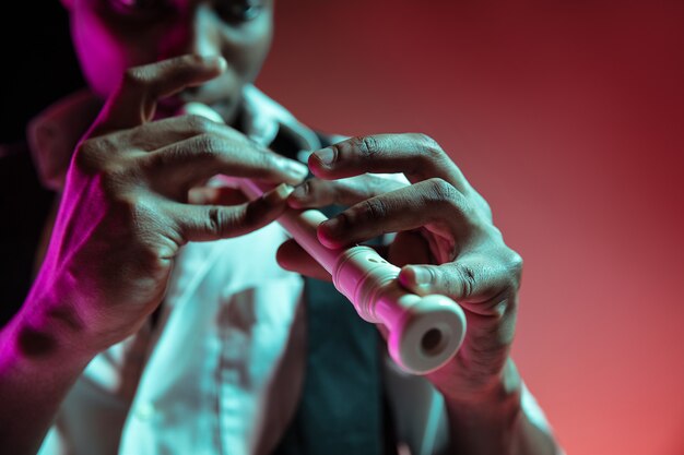 African American handsome jazz musician playing pipe in the studio on a neon background. Music concept. Young joyful attractive guy improvising. Close-up retro portrait.