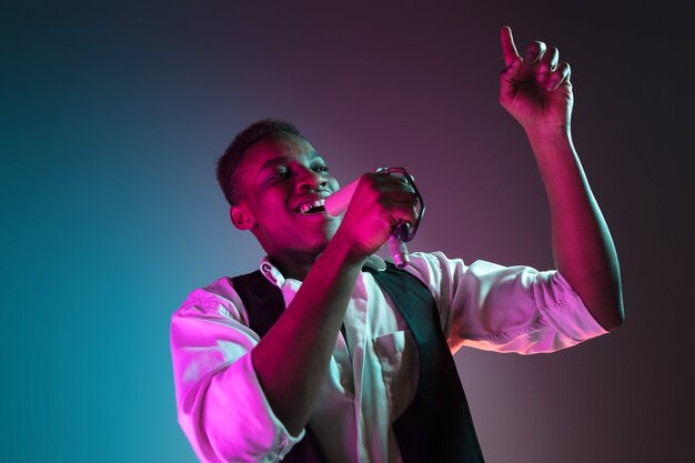 African American handsome jazz musician singing into the microphone in the studio on a neon background. Music concept. Young joyful attractive guy improvising. Close-up retro portrait.