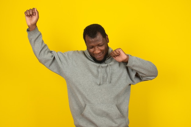An African American happy man is dancing , posing on yellow wall. 