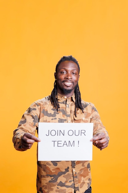 African american hr recruiter holding job offer sign, hiring candidate for business career opportunity standing in studio over yellow background. Advertisement with job application