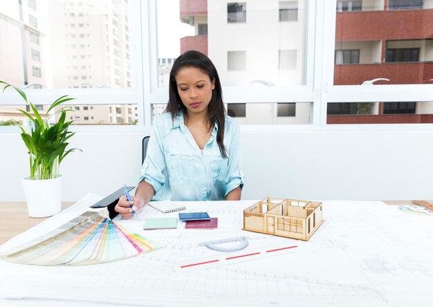 African-American lady on chair taking notes near plan and model of house on table