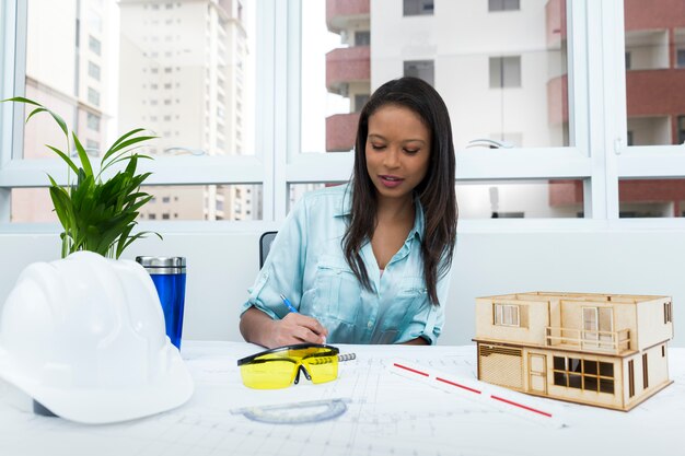 African American lady on chair taking notes near safety helmet and model of house on table