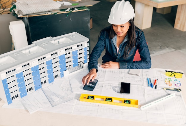 African-American lady in safety helmet sitting near model of building