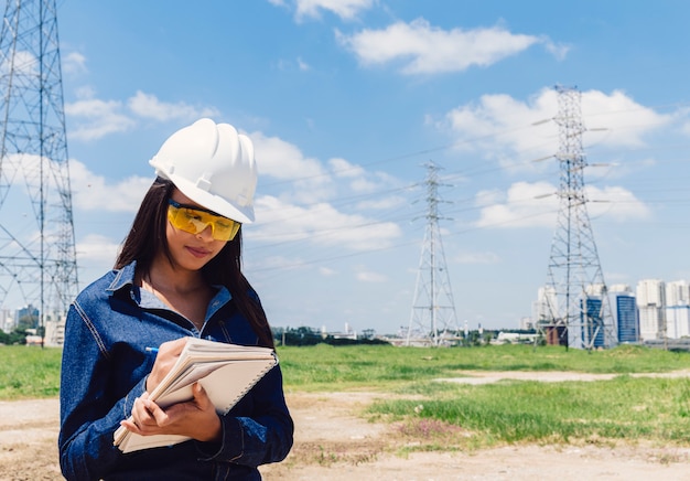 African American lady in safety helmet taking notes near high voltage line