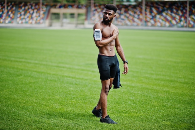 African american male athlete sexy sport bare torso man with running sports arm case for mobile phone posed at green grass of football stadium