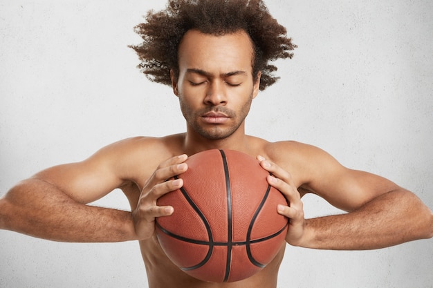 African American male closes eyes, tries to concentrate as holds basket ball