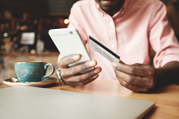 African American man in casual shirt paying with credit card online while making orders