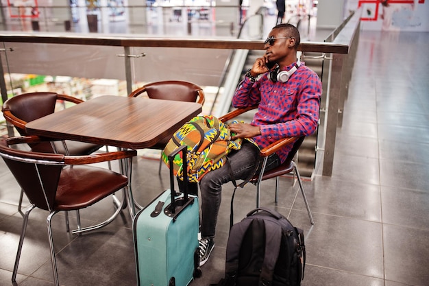 スーツケースとバックパック付きの市松模様のシャツのサングラスとジーンズのアフリカ系アメリカ人男性免税店の黒人旅行者