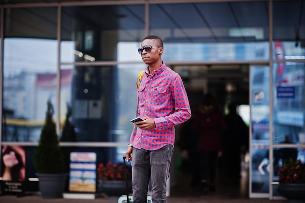 Африканский американец в клетчатой рубашке с чемоданом и рюкзаком Черный путешественник против автовокзала