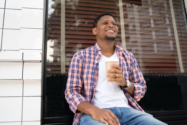 コーヒーショップの外に座ってコーヒーを飲むアフリカ系アメリカ人の男性。アーバンコンセプト。