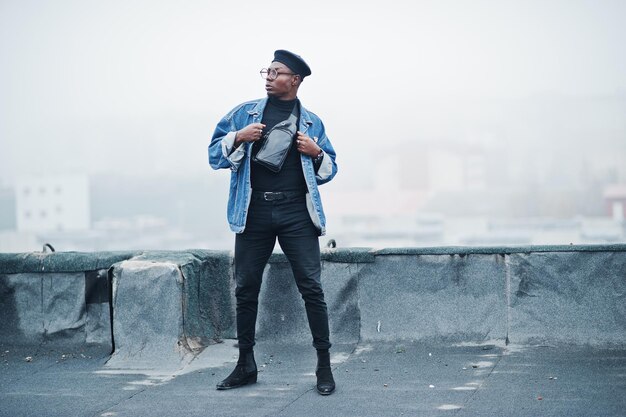 African american man in jeans jacket beret and eyeglasses posed on abandoned roof