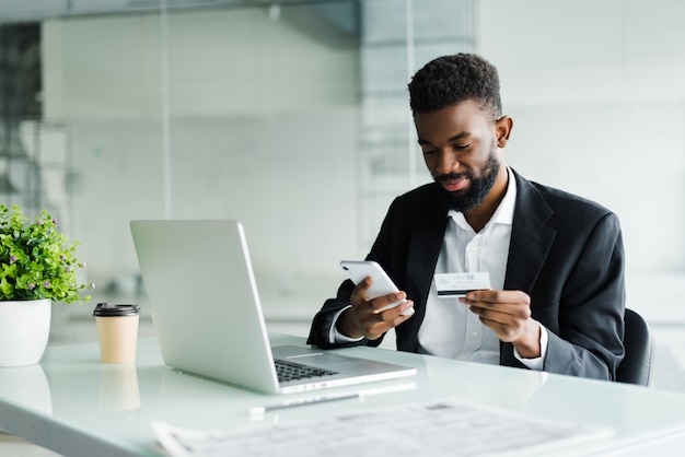 African american man paying with credit card online while making orders via mobile internet making transaction using mobile bank application.